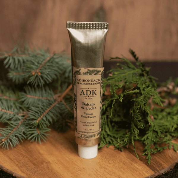 Tube of lotion infront of a wooden background with balsam and cedar branches